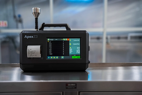 Une photographie stylisée d'un compteur de particules en suspension dans l'air portable ApexZ dans une salle blanche.