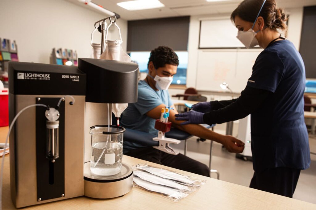 infirmière et patient dans une chambre d'hôpital portant des masques avec un échantillonneur de lots liquides dans la chambre